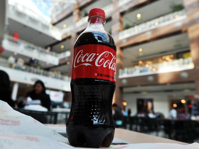 (FILES) In this file photo a bottle of Coca Cola is pictured as people have lunch at a shopping mall in Arlington, Virgina, on February 15, 2011. - Coca-Cola will soon begin selling sodas in completely recycled plastic in the United States for the first time, the beverage giant said on February 9, 2021.The initial items will be introduced this month in a group of states that includes California and Florida, for items such as Coke and Diet Coke in 13.2-ounce bottles made from 100 percent recycled plastic. (Photo by Jewel SAMAD / AFP)