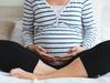 Pregnant woman in striped t-shirt sitting on the bed touching her belly and relaxing. Close up