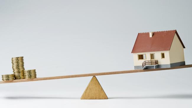 Model house and money coins balancing on a seesaw