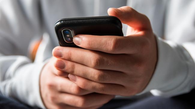 Stock image of Close up of hands of teen boy in white sweater texting on phone.Credit >Getty