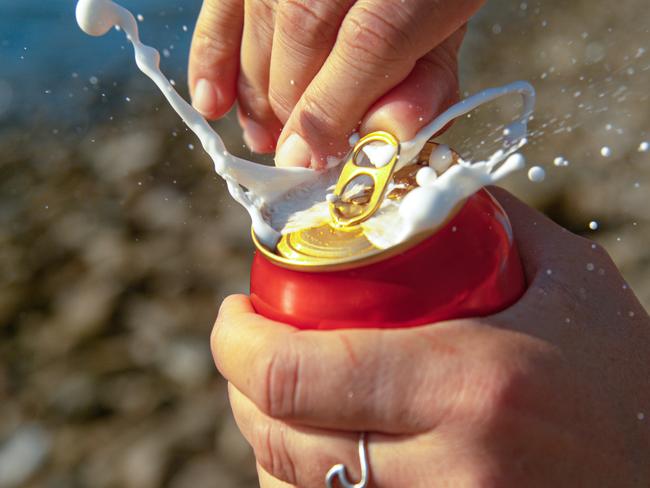 MACRO, DOF: Unrecognizable woman relaxing on the beach during vacation opens up a shaken can of beer and gets sprayed with cold foam. Detailed shot of female tourist's hands opening a stirred beer can