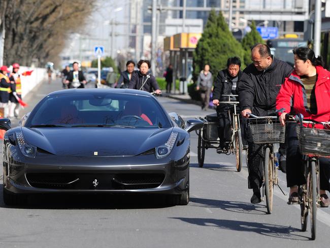 Cyclists ride past and take a look at a Ferrari parked illegally and blocking the bicycle lane off a main road in Beijing on April 7, 2011. China's roads are among the world's most dangerous, with traffic laws and safety widely flouted, but the country's booming auto market has become increasingly important to international auto manufacturers with auto sales rising more than 32 percent in 2010 to 18.06 million units according to the semi-official China Association of Automobile Manufacturers. AFP PHOTO/Frederic J. BROWN