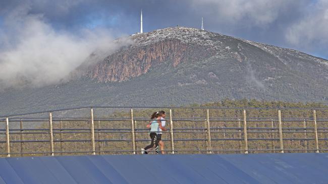 People run along the Bridge of Remembrance at Domain as Kunanyi Mount Wellington is dusted with snow. Picture: Zak Simmonds