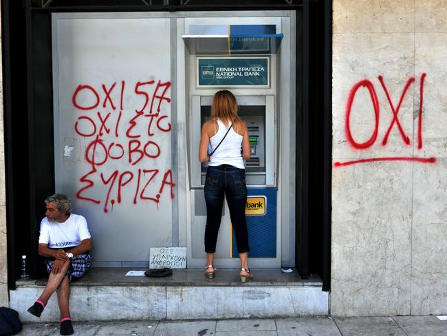 Future uncertain ... A woman withdraws money from an ATM machine next to a beggar and a graffiti reading" No to fear" in Thessaloniki. Picture: AFP/SAKIS MITROLIDIS