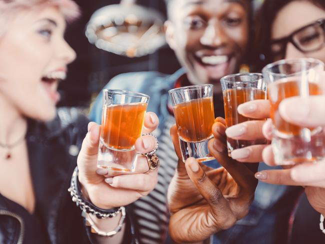 Multi ethnic group of happy friends - caucasian and afro american - drinking shots in the pub. Focus on hands and shot glasses.