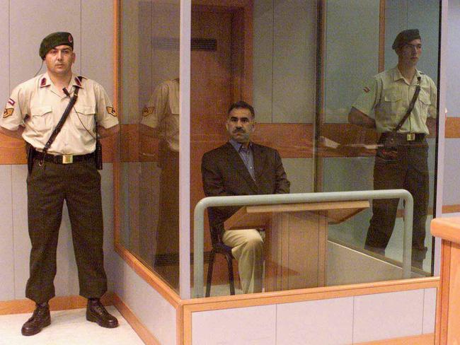 PKK leader Abdulah Ocalan sits behind bulletproof and bombproof glass cubicle guarded by Turkish soldiers at start of his treason trial on prison island of Imrali in 1999.