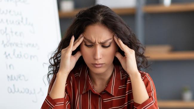 Tired From Work. Portrait of exhausted stressed young woman suffering from headache, touching and massaging her forehead and temples, sitting at desk near whiteboard, thinking about problems