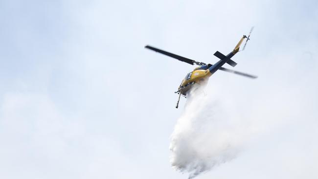 A waterbombing aircraft saturating the fire edge while ground crews extinguish the remnants with hand tools. Picture: WARREN FREY/TFS