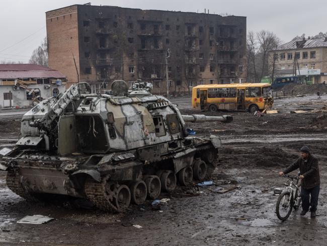 A man pushes his bike through mud and debris past a destroyed Russian tank in front of the central train station that was used as a Russian base in Trostyanets, Ukraine. Picture: Chris McGrath/Getty Images