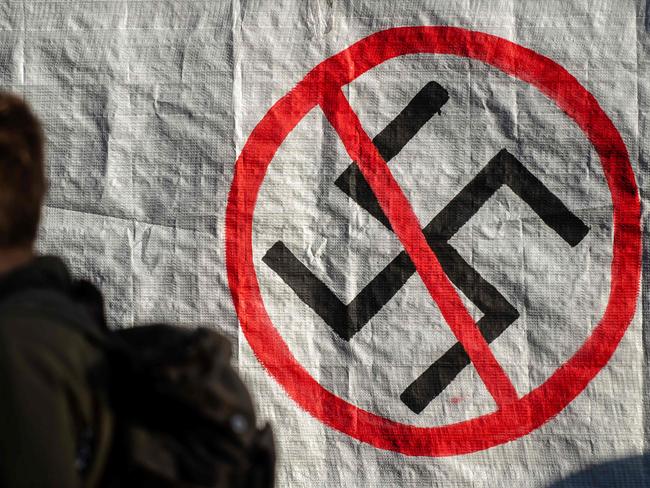 A man walks next to a logo of Nazi swastika during an anti-fascist rally outside the Court of Appeal during the testify of former MP and leader of Golden Dawn party Nikolaos Michaloliakos, on November 6, 2019, in Athens. - The 61-year-old Holocaust denier is one of nearly 70 defendants facing sentences of five to 20 years in prison. The main charge against them is participation in a criminal organisation, in addition to a host of other indictments related to murder and assault. (Photo by Angelos Tzortzinis / AFP)