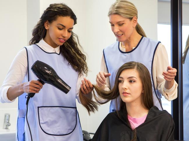 CAREERS: A horizontal image of a hairdresser and trainee hairdresser. The older woman is supervising the younger girl while she is blow drying a customers hair.