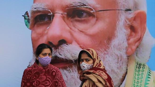 Women don protective masks in front of a poster of India's Prime Minister Narendra Modi outside the All India Institute of Medical Sciences in New Delhi. Picture: Anindito Mukherjee/Bloomberg