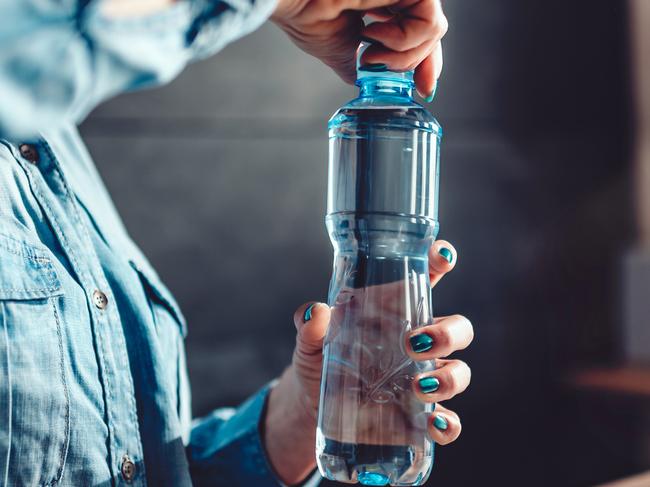 Woman wearing denim shirt working in the office and opening plastic bottle of water