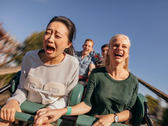 Shot of young friends cheering and riding roller coaster at amusement park. Young people having fun on rollercoaster. generic