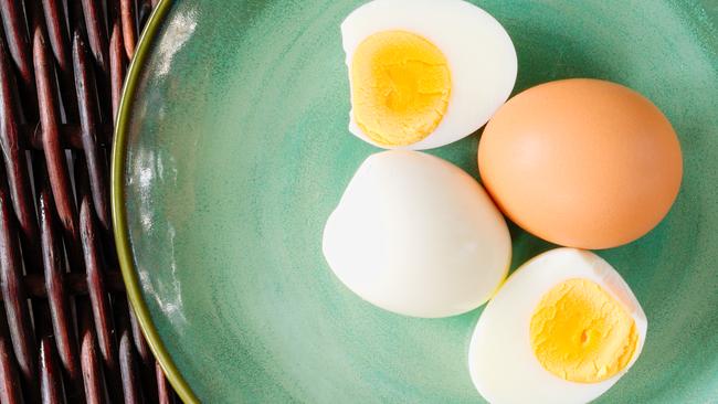 Hard-boiled egg cut and piled on egg slicer and full egg with shell on green plate or dish.