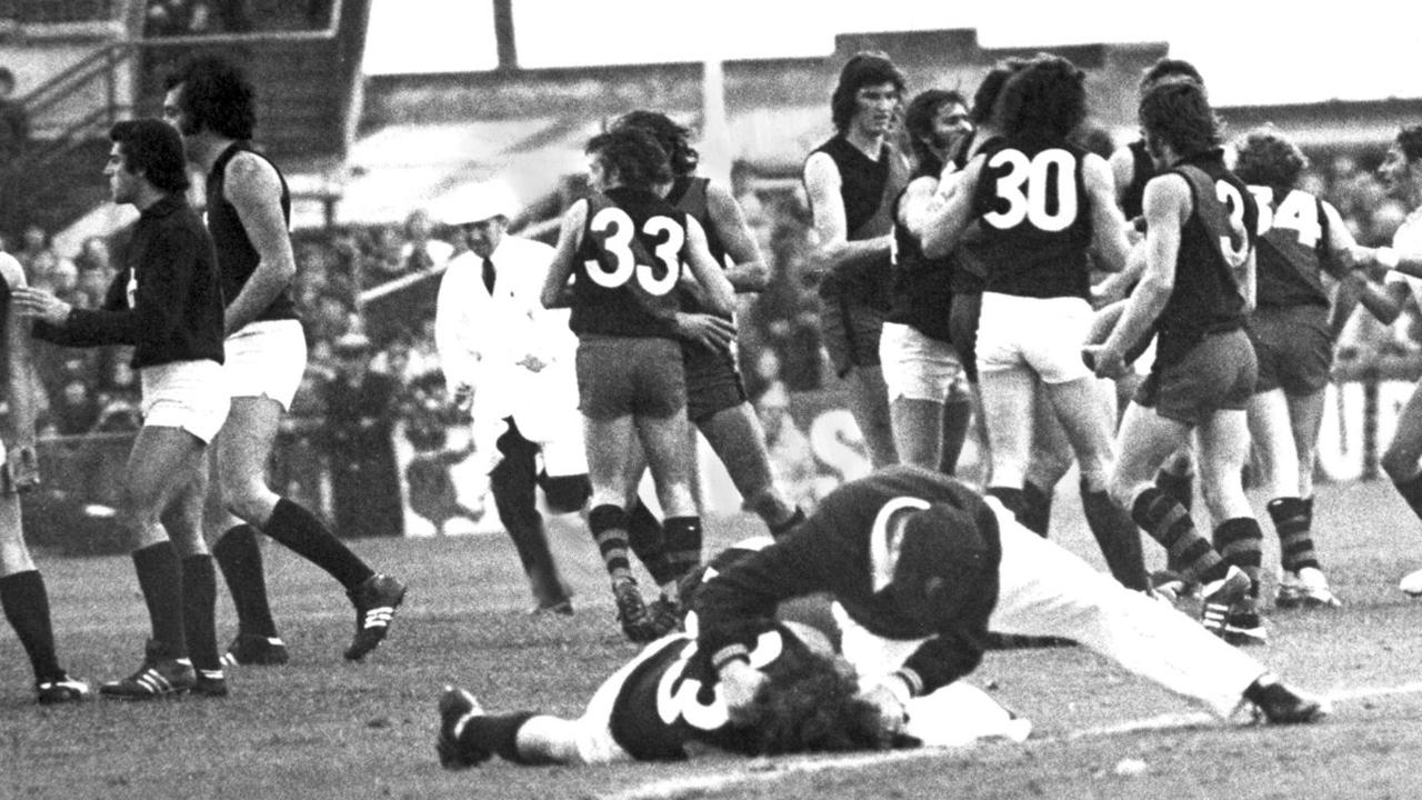 A trainer assists Craig Davis after being knocked out at Windy Hill as a brawl breaks out.