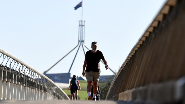 Parliament House is seen in the background as people exercise near Lake Burley-Griffin in Canberra. Picture: Getty Images