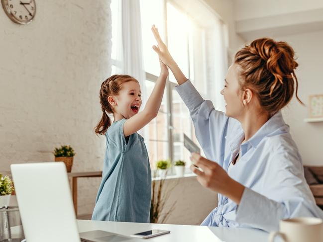 Low angle of excited small daughter giving high five to mother and screaming while celebrating successful online shopping using laptop at table in light living room Picture: Istock
