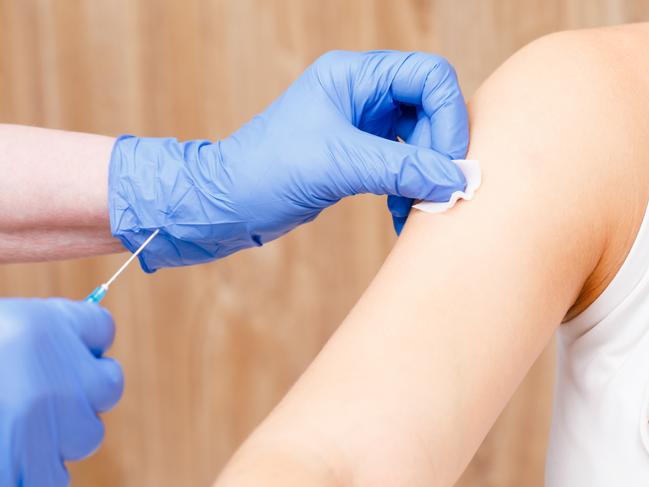 Medical assistant preparing an intramuscular injection of a vaccine disinfecting arm of young woman in a clinic