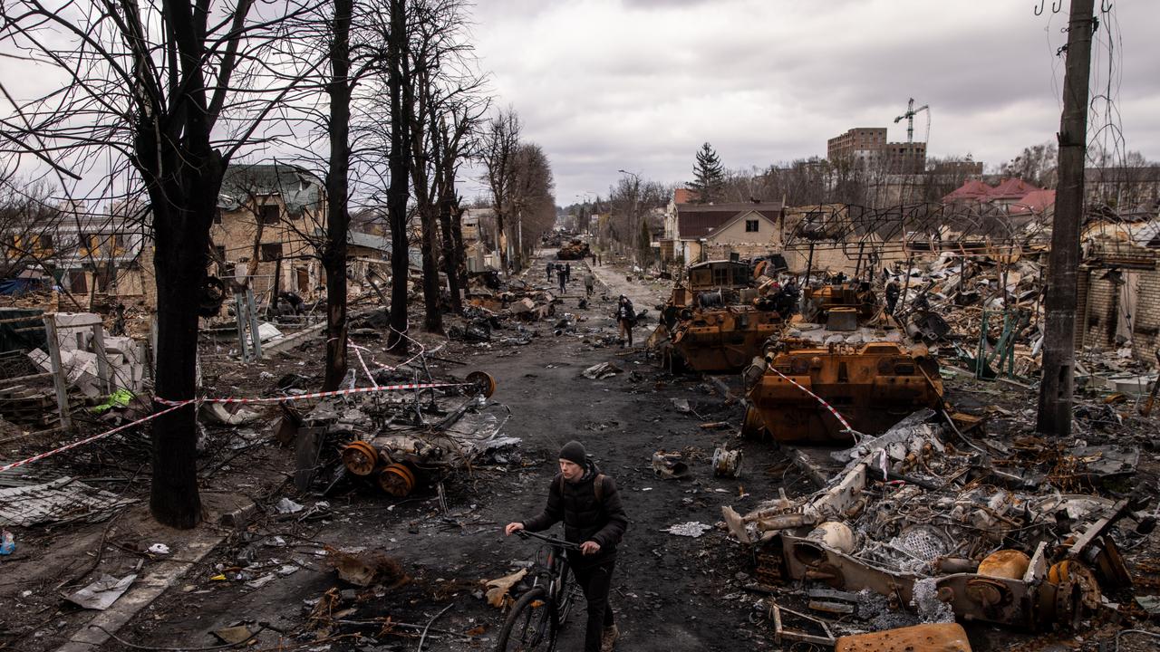 A man pushes his bike through debris and destroyed Russian military vehicles on a street in Bucha. Photo by Chris McGrath/Getty Images