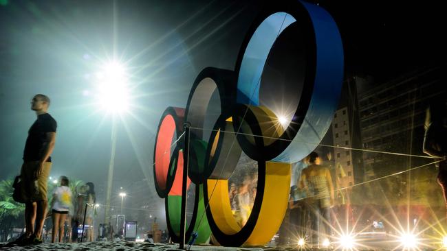 People pose for photographs near to a large Olympic ring display on Copacabana Beach in Rio de Janeiro.