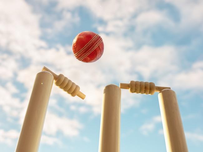 Cricket ball hitting wicket stumps knocking bails out against blue sky background