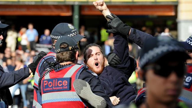 Police move in to remove vegan protesters blocking the intersection of Flinders and Swanston streets. Picture: Andrew Henshaw