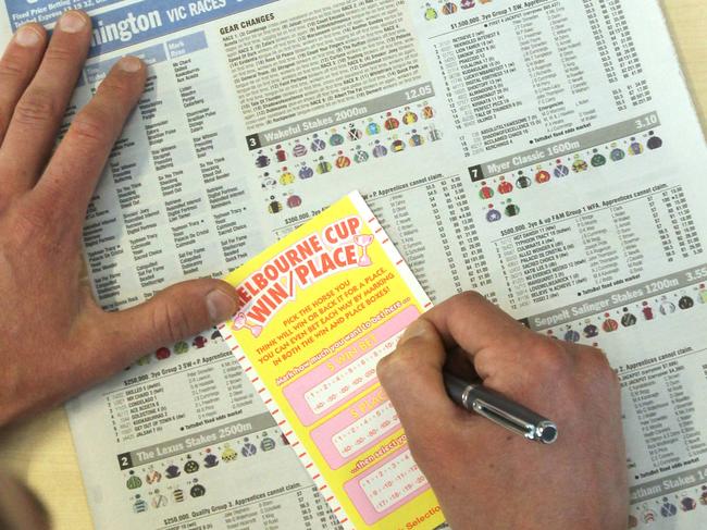 Overhead view of man using the TAB Guide newspaper section to fill out a horseracing betting slip.