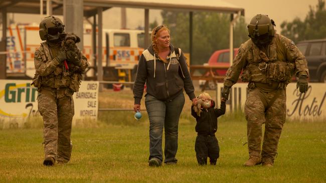 Two Australian Army Soldiers help people evacuate onto an Australian Army CH-47F Chinook helicopter at Omeo showgrounds, Victoria.