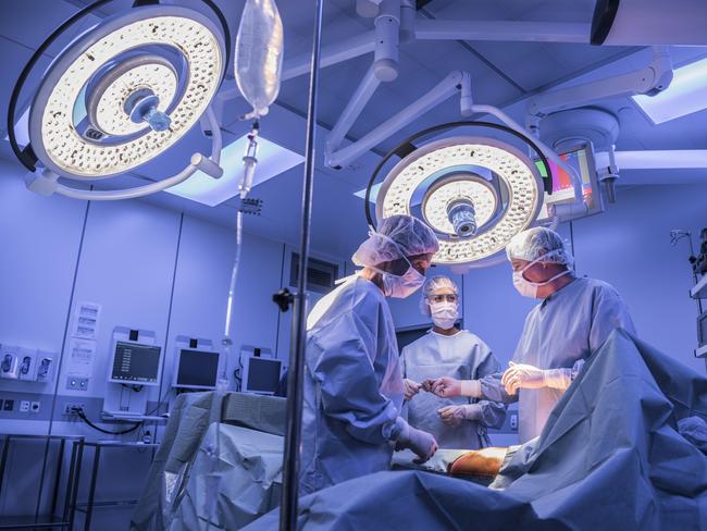 Doctors wearing surgical masks and gowns performing an operation on patient in hospital operating theater.