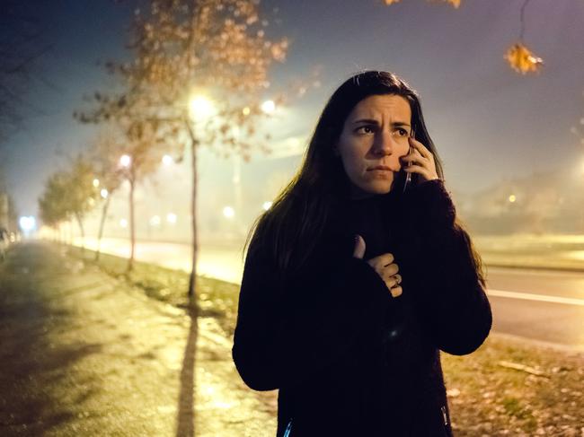 Young woman is using phone, scared of walking down the dark street and surrounded with fog