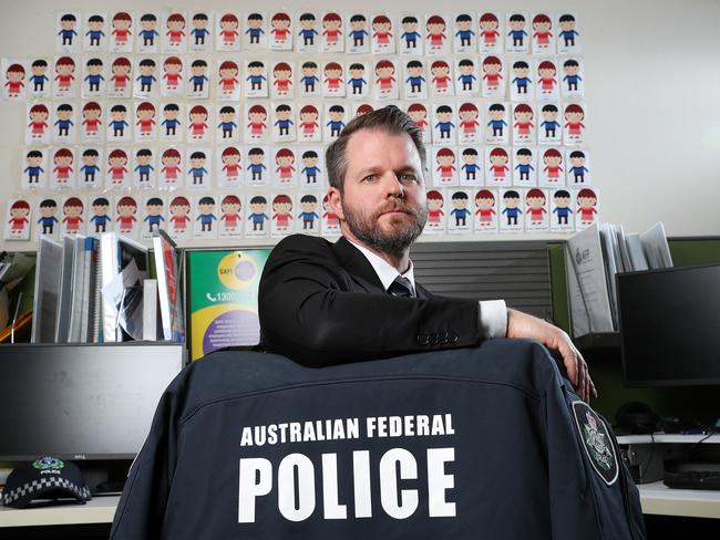 SA JACET senior officer Jonathon Coates in front of a wall of photos of children the unit has saved. Picture: Sarah Reed