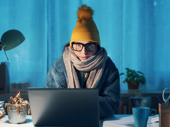 Woman sitting at desk and feeling cold, she is wearing warm clothes and saving money on her utility bills, electricity generic winter