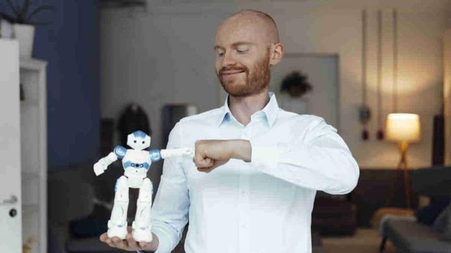 Smiling businessman gesturing fist bump with toy robot standing in office