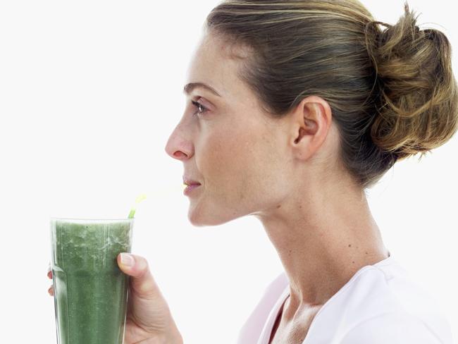 side view of a woman drinking a glass of thick green vegetable juice with a straw