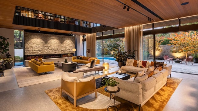 The ground-level living zone blends in moody lighting beneath timber ceilings and looks out onto considered garden views.