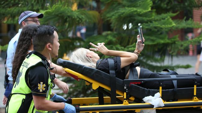 A girl takes a selfie as she is taken away on a stretcher outside the Rolling Loud Festival. Picture: Damian Shaw