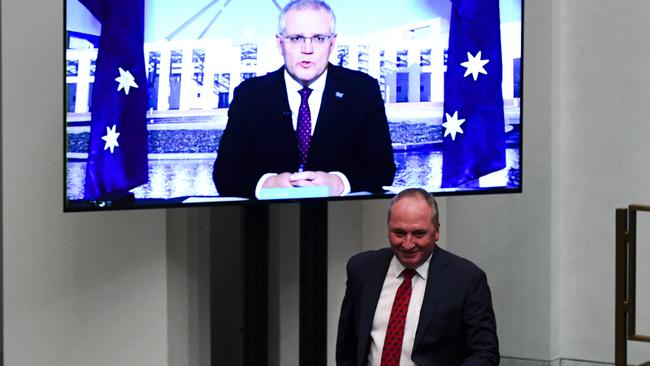 Barnaby Joyce walks past a screen showing Scott Morrison appearing via video link during Question Time.