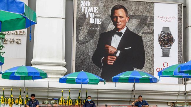 The MGM library of content includes James Bond titles. Security guards sit in the Erawan Shrine compound under an advertisement poster featuring Daniel Craig in the new James Bond movie No Time to Die in Bangkok. Picture: AFP