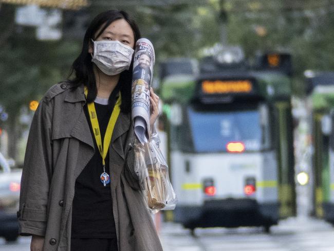 Scenes from Melbourne Australia during the Covid-19 pandemic in 2020. A woman waits for a tram in Melbourne while wearing a protective face mask.