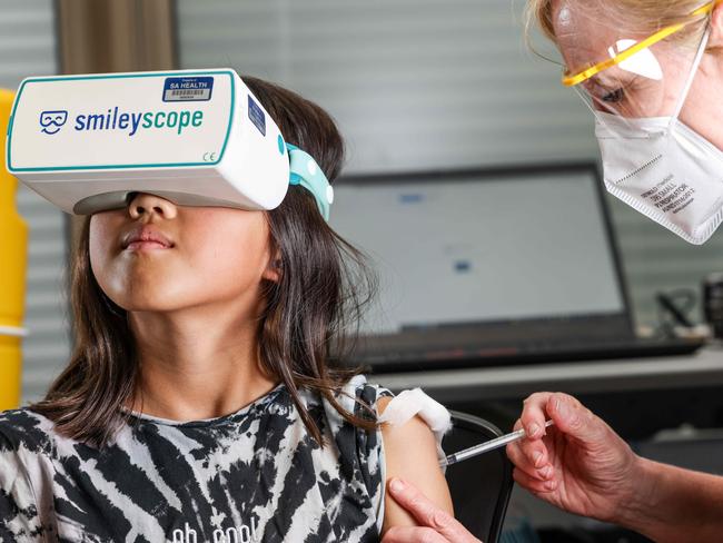 COMMERCIAL-  Nyomi  Meth 9, with a Smileyscope headset about to be vaccinated by nurse Maryanne Attard, Unit Manager at the Adelaide Women and Children Hospital Vax Clinic.IMAGE/Russell Millard