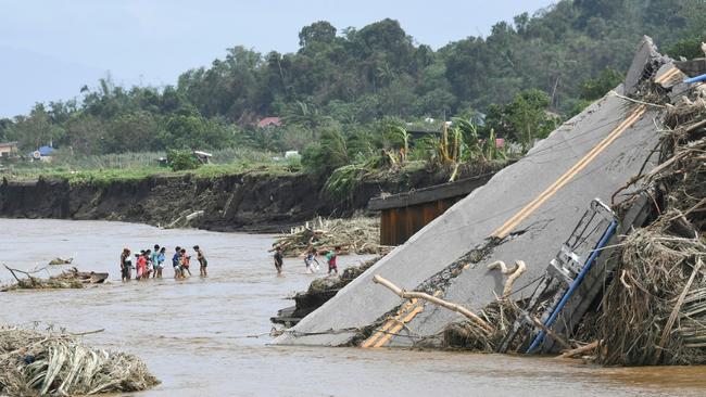 People cross a river next to a bridge that collapsed as the river surged due to rains brought by Tropical Storm Trami in Laurel, Batangas province