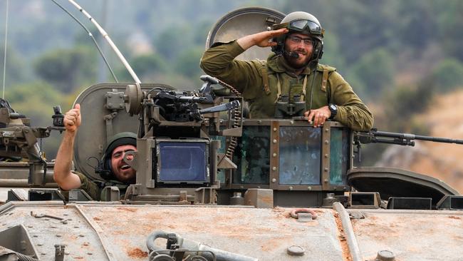 Israeli soldiers gesture in an armoured vehicle as they drive along a street near the northern town of Kiryat Shmona close to the border with Lebanon on October 10, 2023. Israeli forces on October 10 launched artillery fire at Lebanon after rocket fire towards Israel, the army said. (Photo by Jalaa MAREY / AFP)