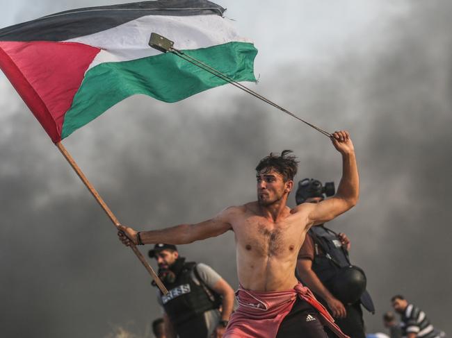 A young protester gripping a Palestinian flag with one hand and swinging a slingshot over his head with the other, on the northern border between Gaza Strip and Israel during protests against the Israeli blockade. Picture: Mustafa Hassona