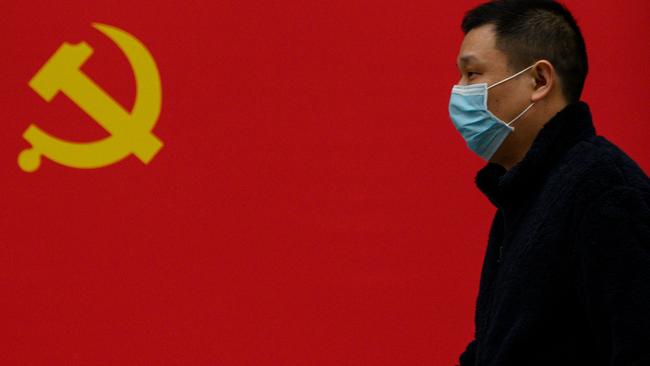 A man wearing a face mask walks past a Communist Party flag in Wuhan. Picture: AFP