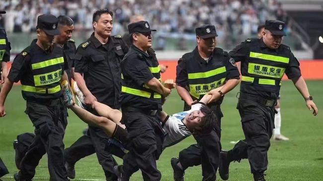 A young Chinese fan is dragged off the field after a pitch invasion.