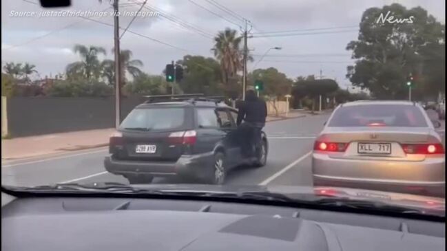 Man sits on car door while driving