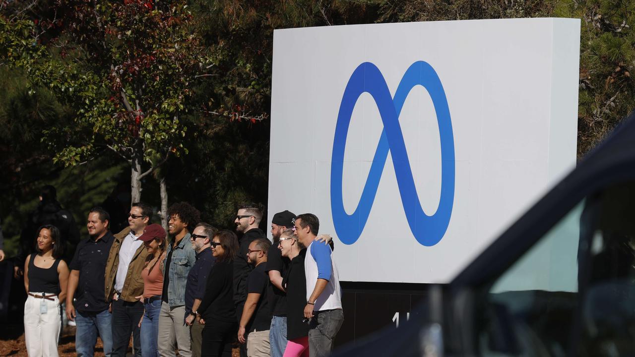 Facebook employees gather in front of a sign displaying a new logo and the name 'Meta' in front of Facebook headquarters in Menlo Park, California.