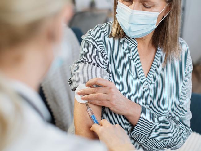 View from the shoulder of female unrecognizable doctor. Senior lady in protective mask, being vaccinated at home by her family gp doctor. Picture: Istock