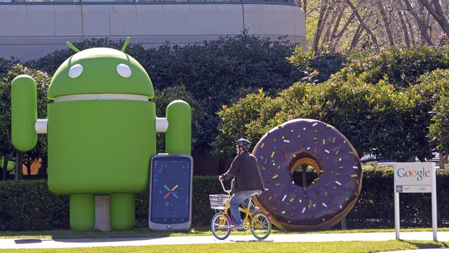 An employee rides a Google bike pool bike past an Android foam robot at the Googleplex.